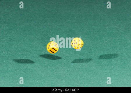 Two yellow dices falling on a green table Stock Photo