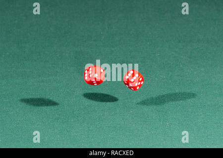 Two red dices falling on a green table Stock Photo