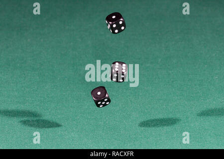 Three black dices falling on a green table Stock Photo