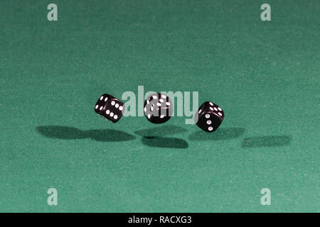 Three black dices falling on a green table Stock Photo