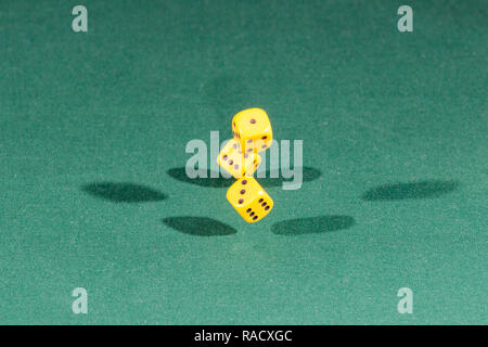 Three yellow dices falling on a green table Stock Photo