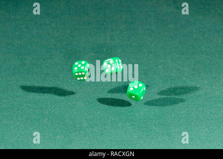 Three green dices falling on a green table Stock Photo