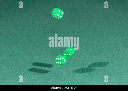 Three green dices falling on a green table Stock Photo