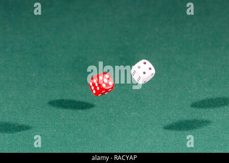 Two red and white dices falling on a green table Stock Photo