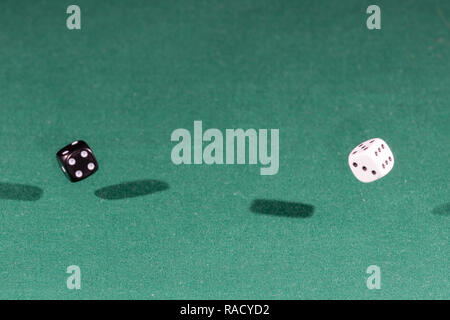 Two white and black dices falling on a green table Stock Photo