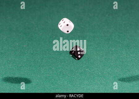 Two white and black dices falling on a green table Stock Photo