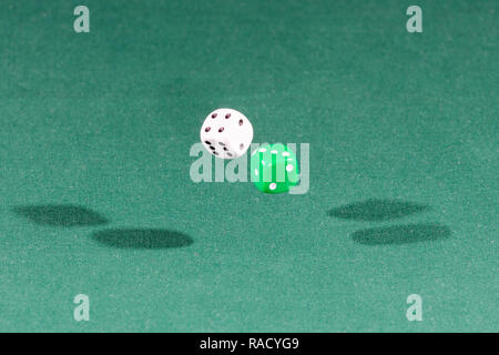 Two white and green dices falling on a green table Stock Photo