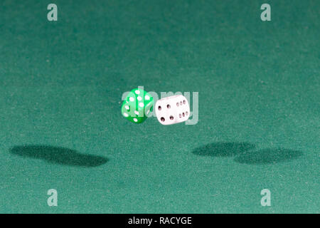 Two white and green dices falling on a green table Stock Photo