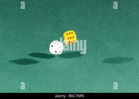 Two white and yellow dices falling on a green table Stock Photo