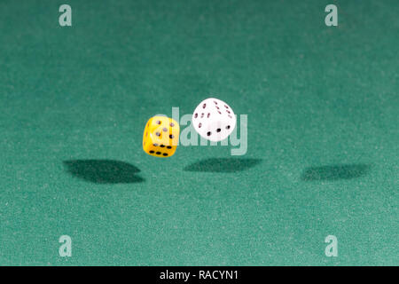 Two white and yellow dices falling on a green table Stock Photo