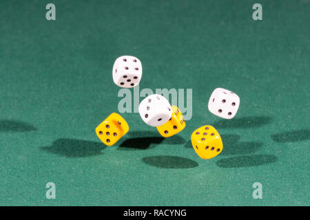 Six white and yellow dices falling on a green table Stock Photo