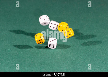 Six white and yellow dices falling on a green table Stock Photo