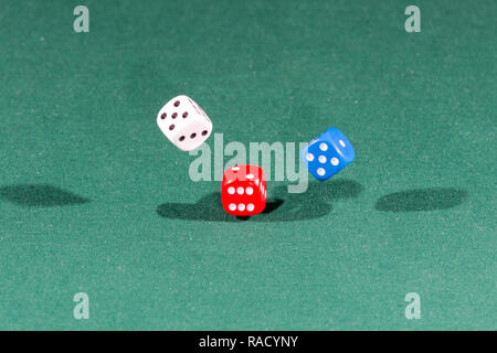White, red and blue dices falling on a green table Stock Photo