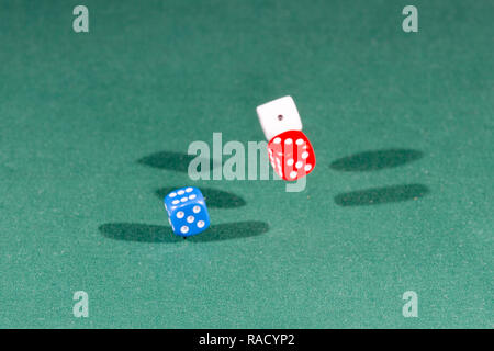 White, red and blue dices falling on a green table Stock Photo