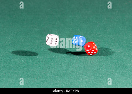 White, red and blue dices falling on a green table Stock Photo