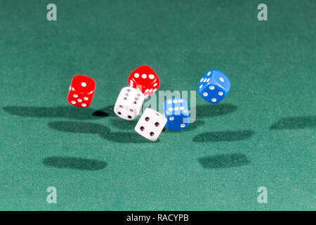 White, red and blue dices falling on a green table Stock Photo