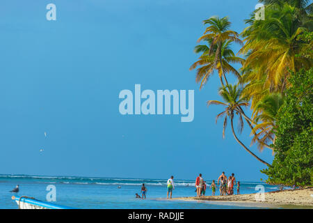 Pigeon Point, Tobago, Caribbean. Family or group of people, strolling along the beach with swaying palm trees, bright blue sky and blue sea. Landscape Stock Photo
