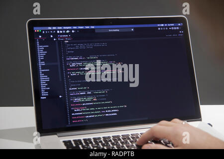 Male programmer working on laptop computer at white desk in office, codding php code Stock Photo