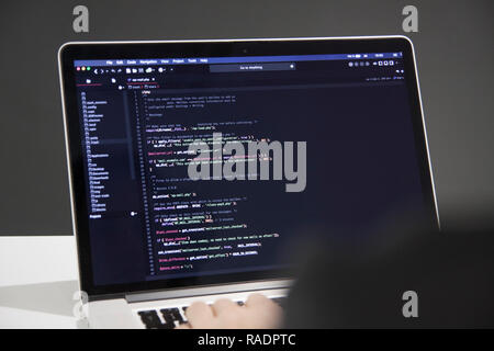 Male programmer working on laptop computer at white desk in office, codding php code Stock Photo
