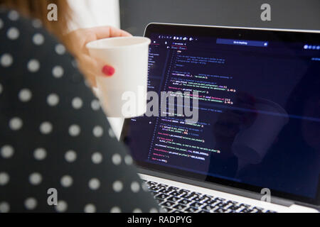 Woman programmer with cup of coffee working on laptop computer in php code at office Stock Photo