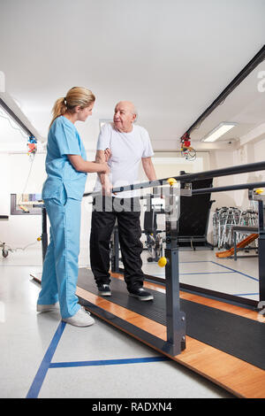 Therapist supports senior man on treadmill while running in rehab Stock Photo