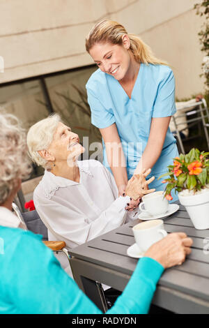 Friendly caregiver with senior women drinking coffee in retirement home Stock Photo