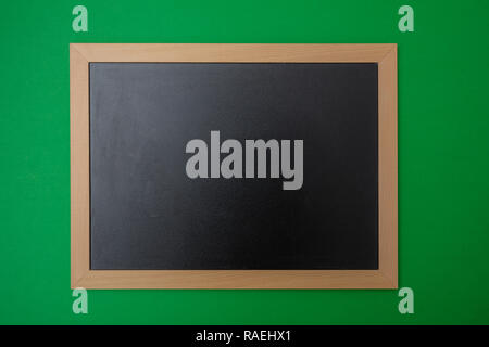 Black blank empty chalkboard with wooden frame, green wall background. Space for text Stock Photo