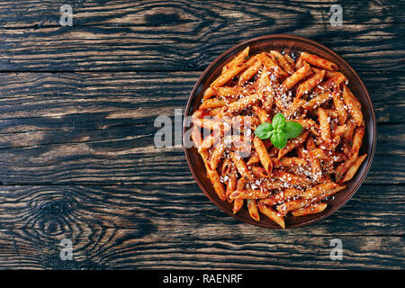 classic italian penne arrabiata  in a clay bowl with basil and freshly grated peccorino cheese on a rustic wooden table, view from above, flatlay, cop Stock Photo