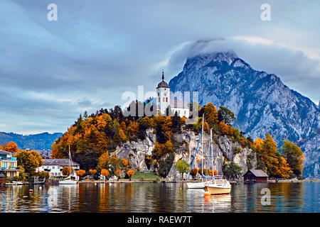 Beautiful scenic sunset over Austrian alps lake. Boats, yachts in the sunlight infront of church on the rock with clouds over Traunstein mountain at t Stock Photo