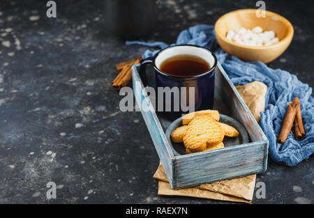Blue enamelled cup of tea, cinnamon sticks, anise stars and shortbread on a dark background. Space for text. Stock Photo