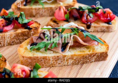 Selection of tasty Italian bruschetta or canapes on toasted baguette topped with tomatoes, Prosciutto di Parma, arugula and balsamic glasse sauce on c Stock Photo