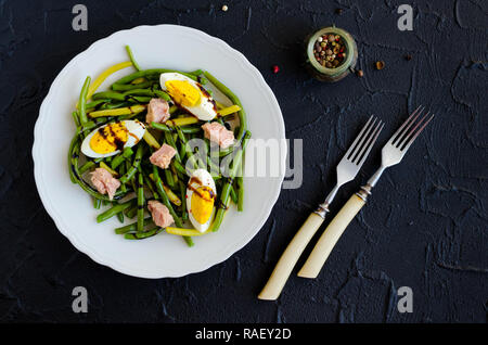Fresh summer warm salad with cooked green beans, tuna, boiled eggs and sauce balsamico glassa in white plate on black stone background. Healthy eating Stock Photo