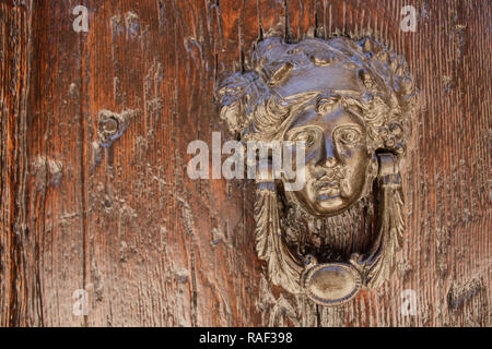 Door knocker in the form of a girl's head with grape leaves on a wooden door Stock Photo