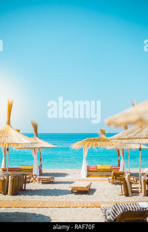 Sunshade umbrellas and deckchairs on the beautiful beach in Himara, Albania. Stock Photo