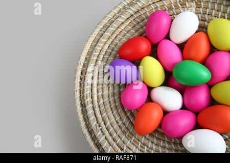 Brightly colored easter eggs, in a straw basket against a grey background. Stock Photo