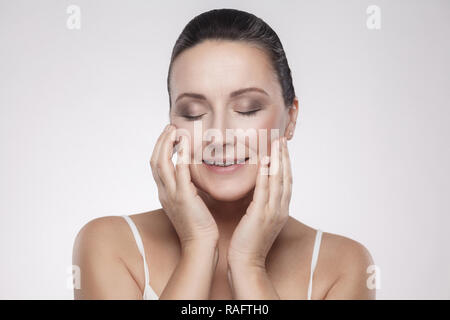Portrait of happy smiling charming, beautiful woman touching skin or applying cream, with perfect skin after cream, balm, mask, lotion, isolated on gr Stock Photo