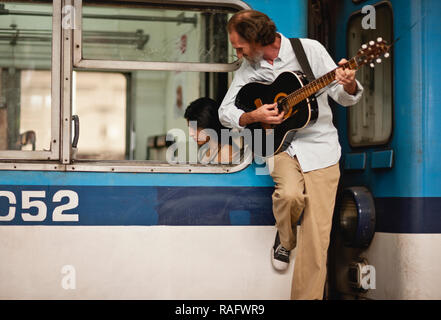 Man leaning on subway car playing guitar while checking out a female passenger. Stock Photo
