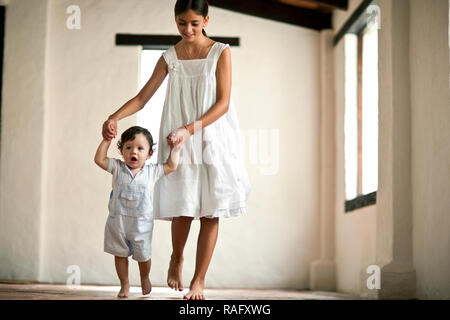 Young girl helping baby brother walk as she holds his hands. Stock Photo