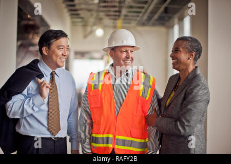 Two smiling business colleagues discuss building plans with the construction site foreman. Stock Photo