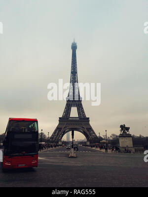 A red tourist bus on the pavement road in front of the famous Paris landmark Eiffel Tower view from the street. Stock Photo