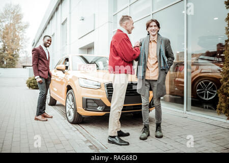 Stylish mature father wearing red jacket presenting car to his son Stock Photo