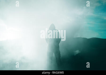 A hooded figure silhouetted by the sun as smoke surrounds him Stock Photo