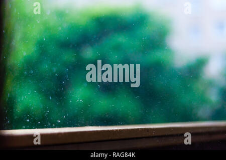 Summer rain raindrops falling down on wooden painted handle of balcony railings on blurred trees background Stock Photo