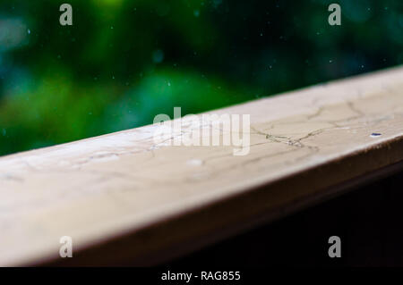 Summer rain raindrops falling down on wooden painted handle of balcony railings on blurred trees background Stock Photo