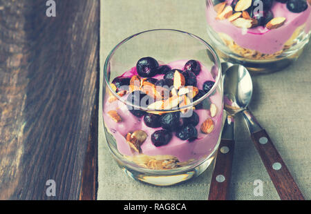 Dessert of oatmeal, banana, yogurt, blueberries and almond in glass bowls on rustic wooden background. Vintage toned picture. Stock Photo
