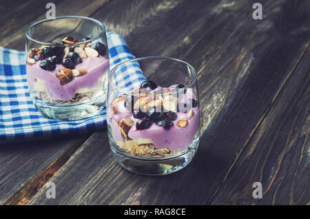 Dessert of oatmeal, banana, yogurt, blueberries and almond in glass bowls on rustic wooden background Stock Photo