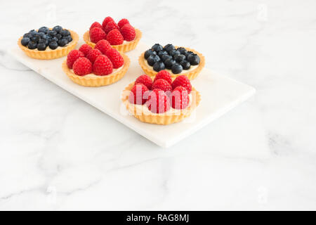 Homemade blueberry and raspberry and tarts on white marble board and background with copy space. Stock Photo
