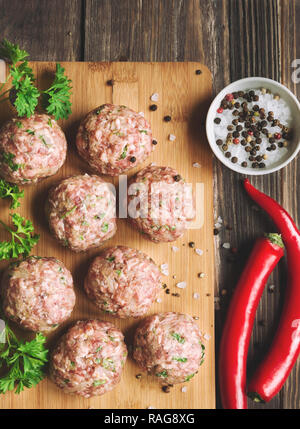 Raw meatballs with parsley and chili peppers on rustic wooden background. Top view. Stock Photo