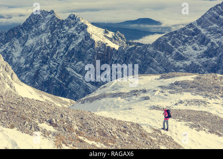 Female alpinist descending into mountain valley crossing flakes of snow. Stock Photo