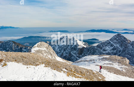 Female alpinist descending into mountain valley crossing flakes of snow. Stock Photo